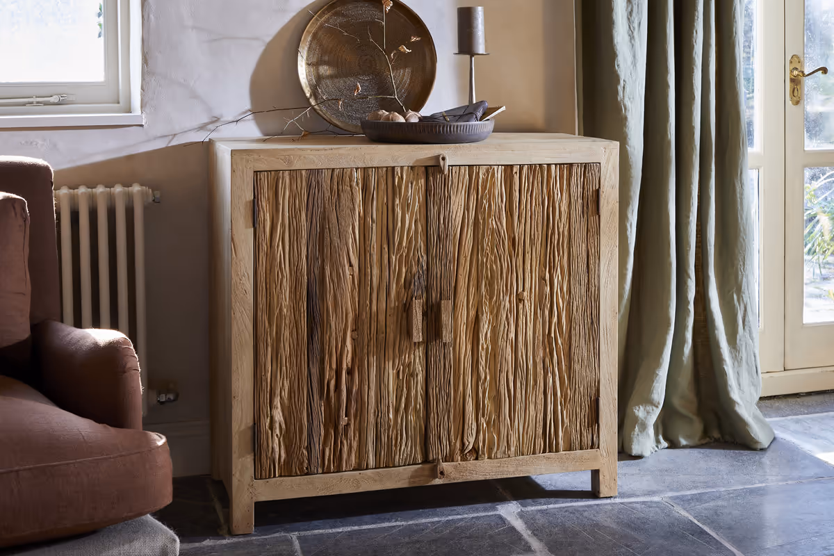 Tamia reclaimed wood cabinet in natural colour styled with home decor on top of it and a brown armchair.