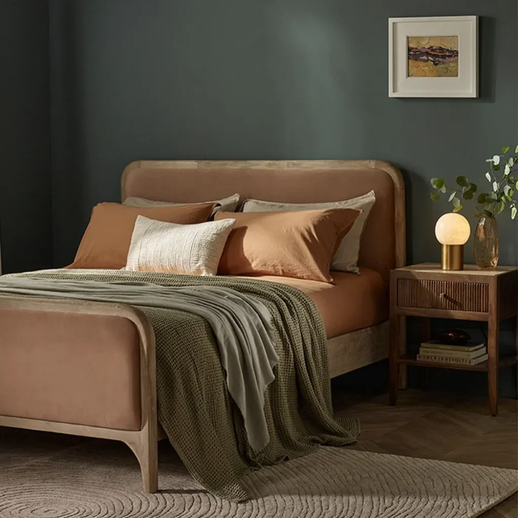 bedroom with velvet bedframe, navy walls and brass bedside light.