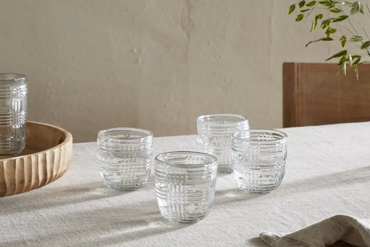 The Honest Nkuku Recycled Glassware Review: We Look At 10 Tumblers, Highballs and Gin Glasses four clear glass patterned tumblers made from recycled glass on a linen table cloth