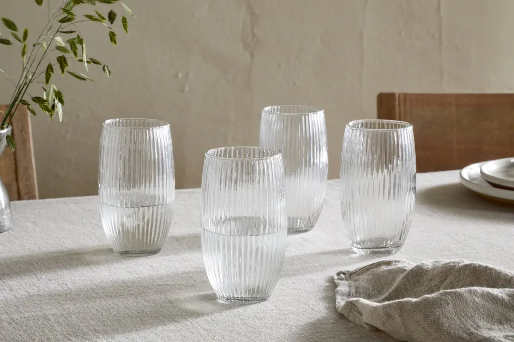 The Honest Nkuku Recycled Glassware Review: We Look At 10 Tumblers, Highballs and Gin Glasses four ridged clear glass tumblers made from recycled glass on a linen tablecloth