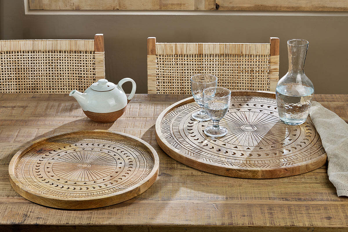 The Honest Nkuku Recycled Glassware Review: We Look At 10 Tumblers, Highballs and Gin Glasses mango wood tray with an indian design engraved with a teapot and clear glasses set on a wooden table with rattan chairs