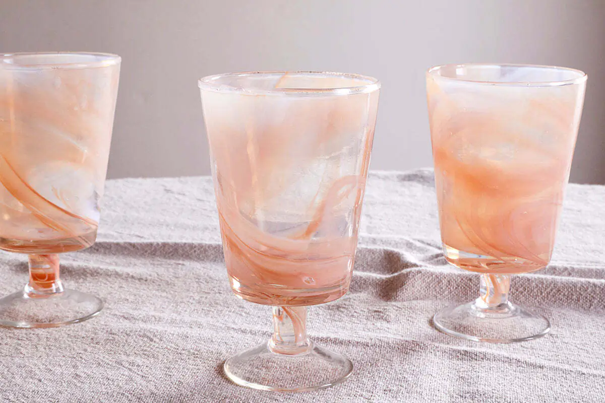 The Honest Nkuku Recycled Glassware Review: We Look At 10 Tumblers, Highballs and Gin Glasses close up of wine glass with an apricot marble swirl pattern through it