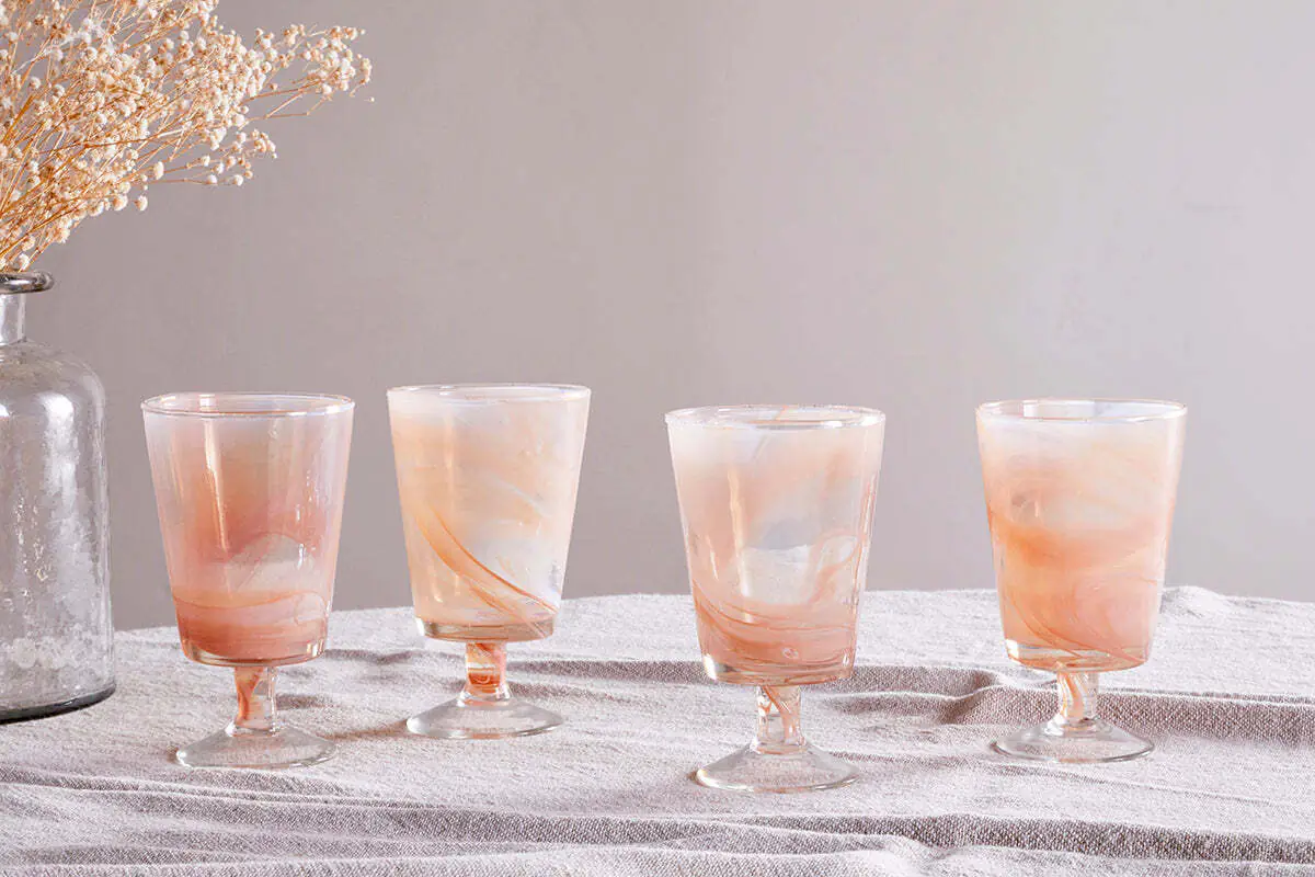 The Honest Nkuku Recycled Glassware Review: We Look At 10 Tumblers, Highballs and Gin Glasses four wine glasses set on a linen table cloth all with an apricot coloured marble swirl going through them