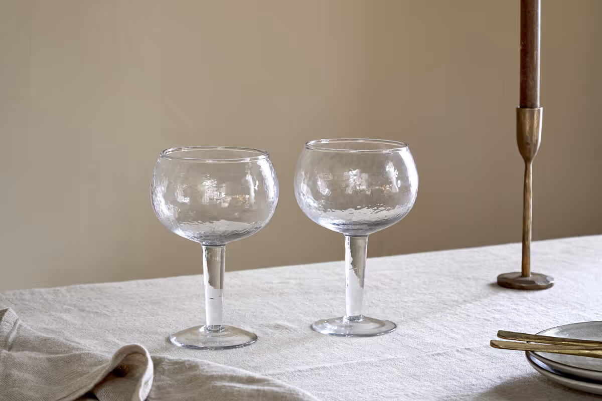 The Honest Nkuku Recycled Glassware Review: We Look At 10 Tumblers, Highballs and Gin Glasses two gin glasses in a clear glass with a hammered pattern set on a linen tablecloth