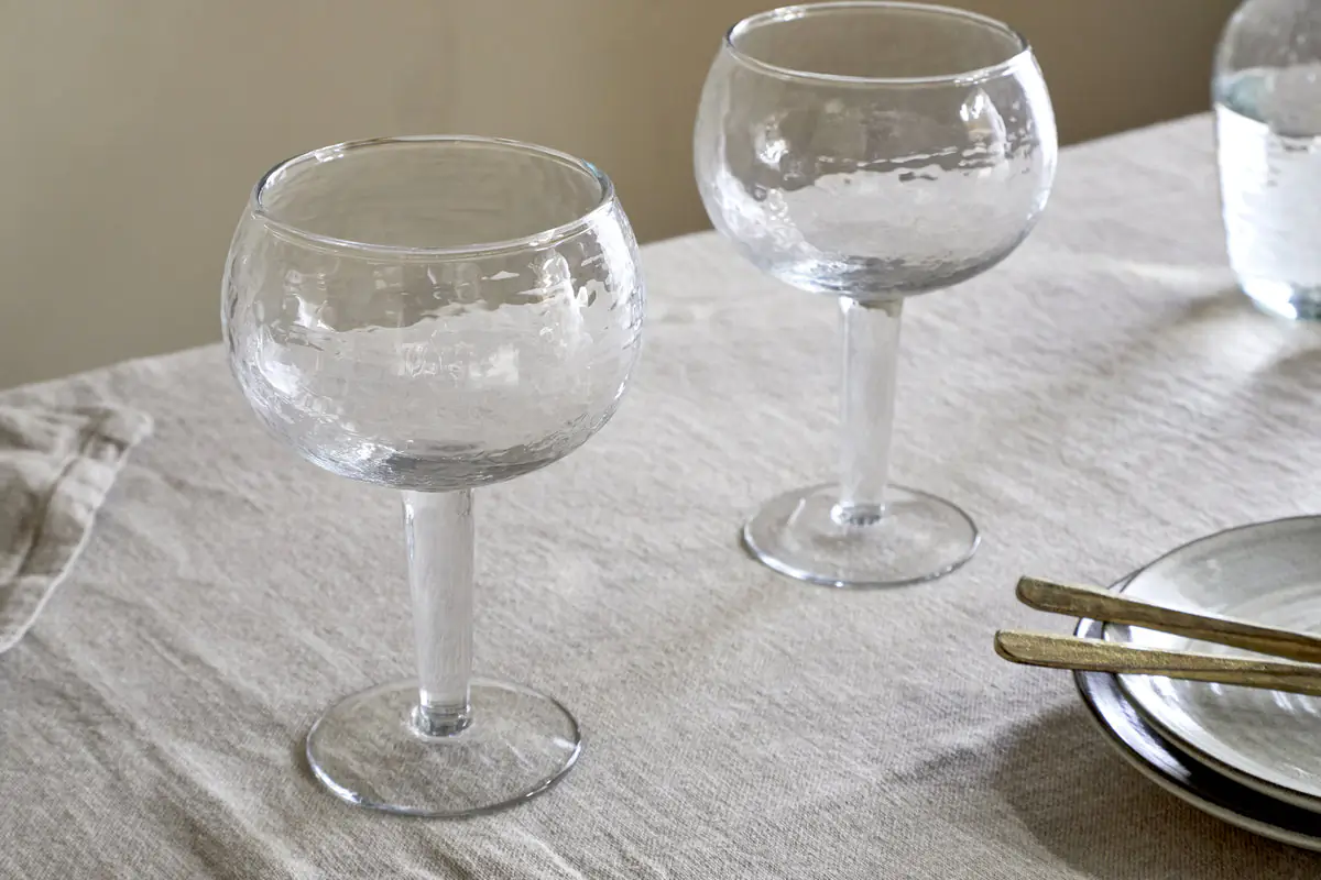 The Honest Nkuku Recycled Glassware Review: We Look At 10 Tumblers, Highballs and Gin Glasses close up shot of two gin glasses set on a linen tablecloth with a hammered pattern