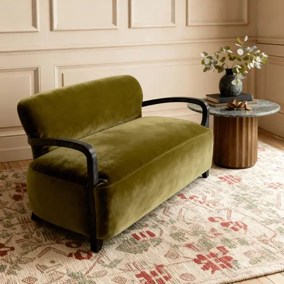 An olive green velvet loveseat with black arm rests by atkin and thyme.