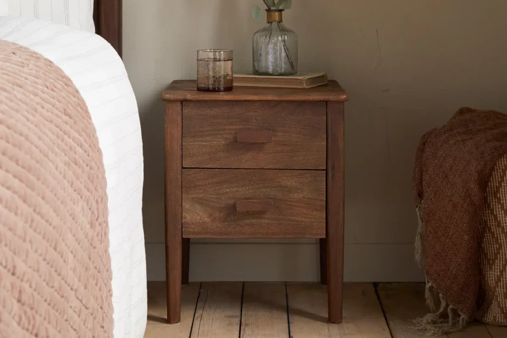 How to Create a Sustainable Bedroom: A Practical Guide Anbu Acacia Bedside Table in Washed Walnut styled beside a bed and with a recycled glass tumbler on top.