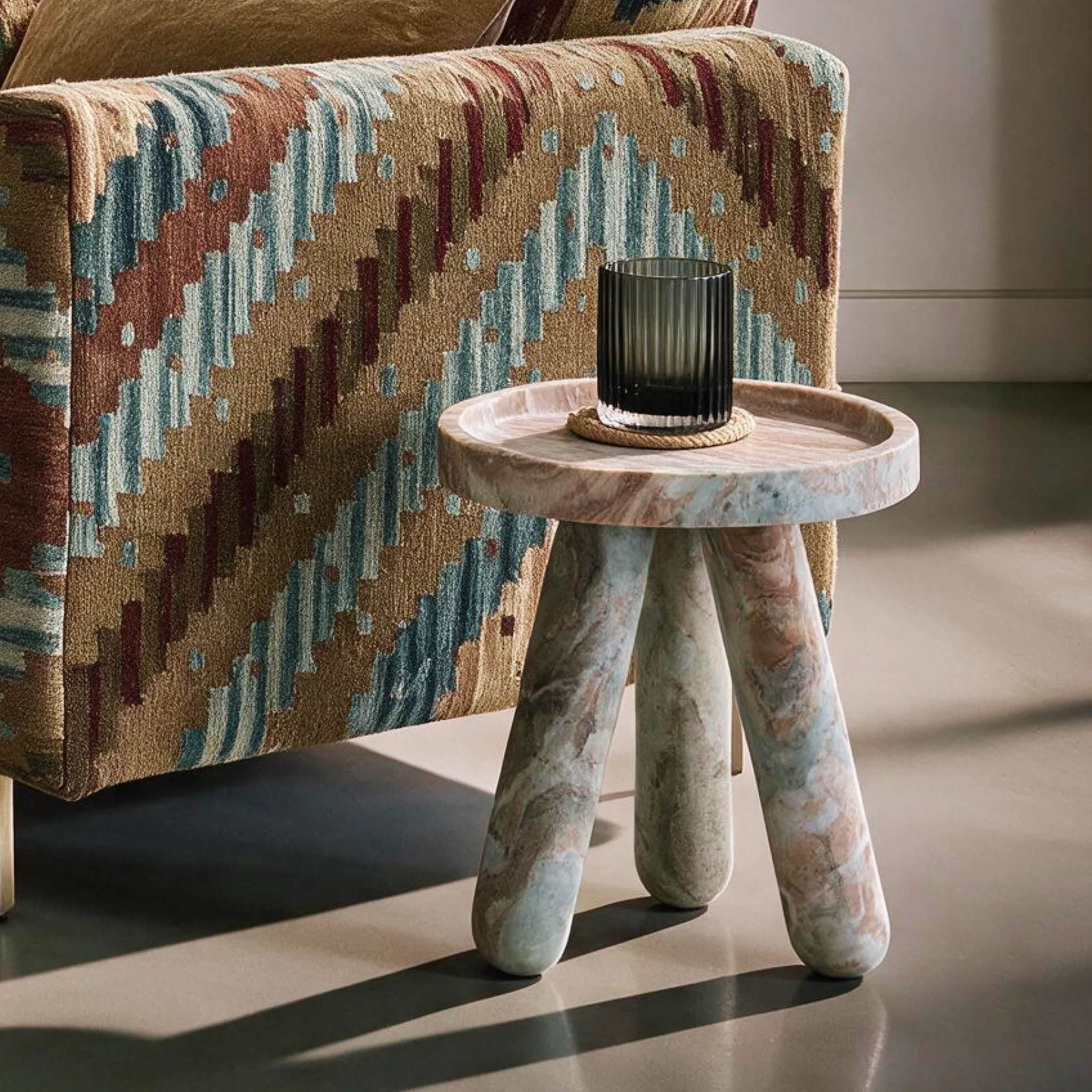 Marble side table with three legs and circular top beside a patterned sofa.