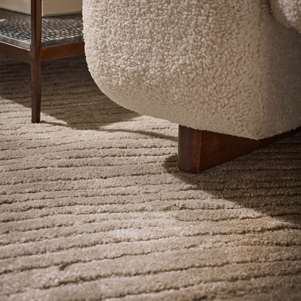 Kayo hand tufted rug in cream colour with a boucle chair close up.