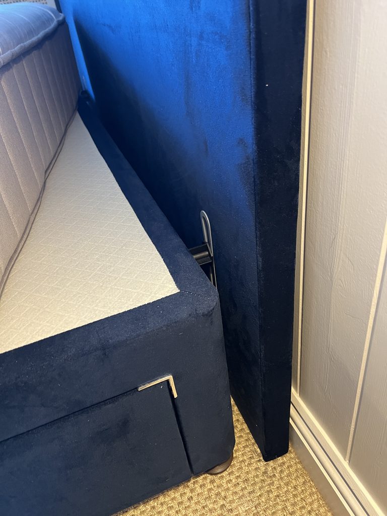 Close up view of the attachment of the headboard to the bed frame of a navy velvet Simba Sleep bed.