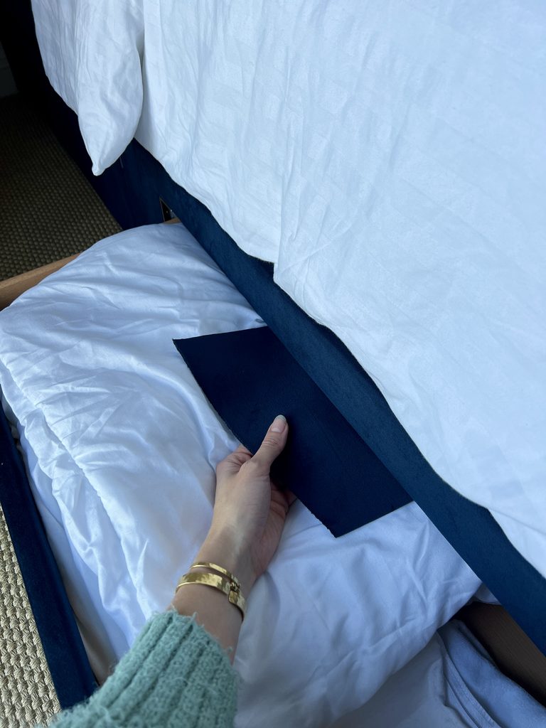 A hand holding some fabric with an open draw with bedding beneath it.
